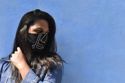 Portrait of young woman standing against blue wall