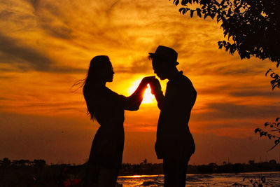 Silhouette couple standing against orange sunset sky