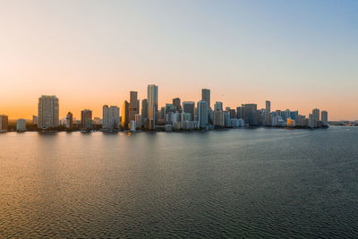 Sea by buildings against clear sky during sunset