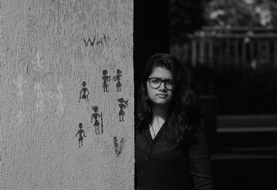 Portrait of young woman standing by wall