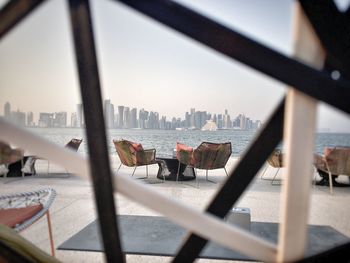 View of city seen through railing by sea against sky