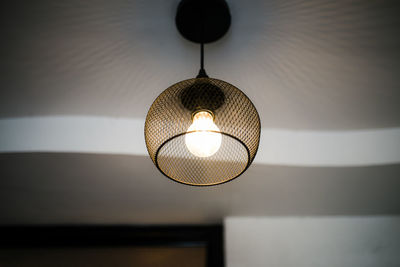 Low angle view of illuminated light bulb hanging from ceiling