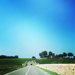 Road amidst field against clear blue sky