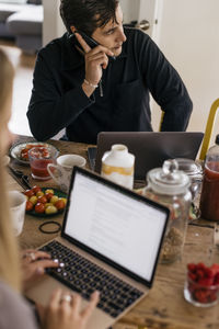 Male freelancer talking on smart phone while sitting with breakfast on table at home