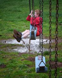 Side view of boy playing on swing at park during rainy season