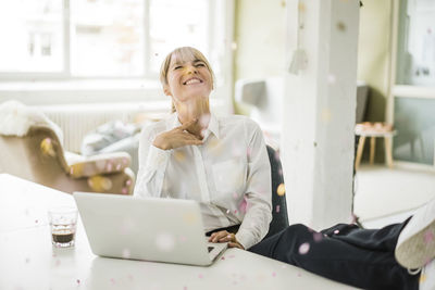 Confetti falling on businesswoman with laptop in office