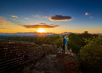 Man standing on great wall of china against cloudy sky during sunset
