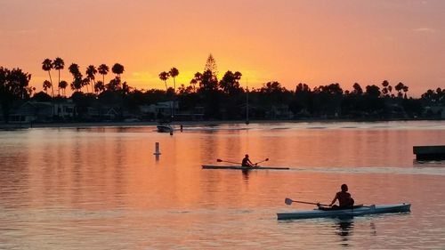 People on lake against sky during sunset