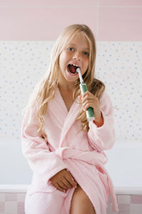 Smiling cute girl in a pink bathrobe brushes her teeth in a bathroom hygiene concept