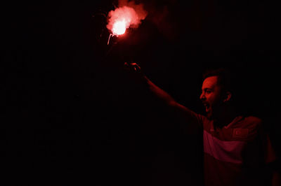 Man holding distress flare screaming while standing against black background