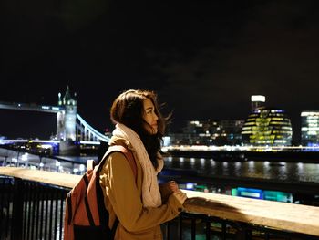 Woman looking at illuminated cityscape against sky at night