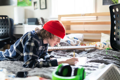 Teenage boy working on homework in bedroom surrounded by belongings