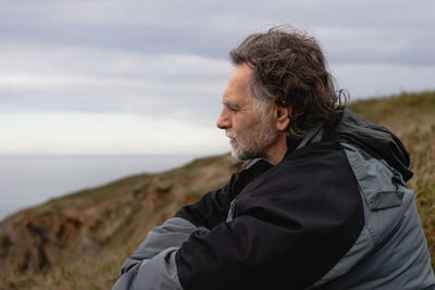 Side view of man looking away while sitting on mountain against sky