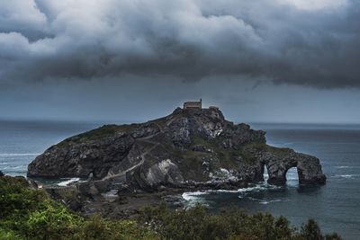 Lighthouse on rocks by sea against sky