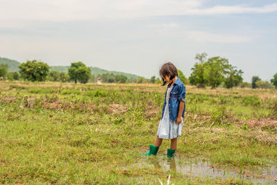 Rear view of boy standing on field against sky