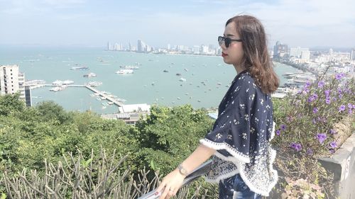 Woman standing by sea against cityscape