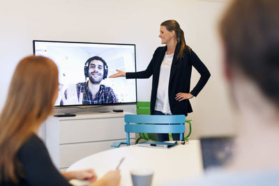 Happy businesswoman introducing partner to colleagues during conference call in board room