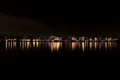 Illuminated buildings by river against sky at night