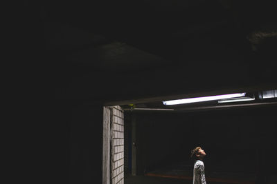 Side view of boy standing below illuminated ceiling in darkroom