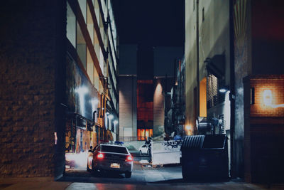 Cars on illuminated street amidst buildings at night