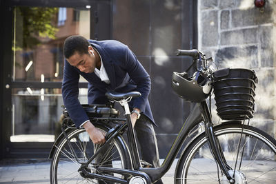 Young male commuter locking electric bicycle against building in city