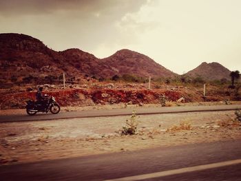 Man riding motorcycle on road against mountain range