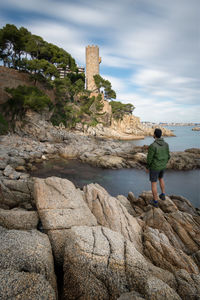 Rear view of woman standing on rock against sky