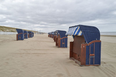 Hooded beach chairs on sand against sky