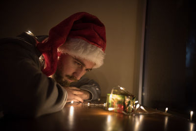 Close-up of young man by illuminated christmas lights on gift in darkroom