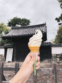 Hand holding ice cream cone against building