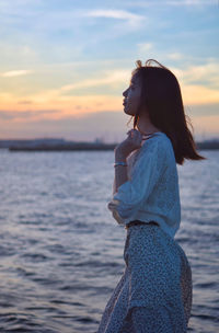 Woman standing by sea against sky during sunset