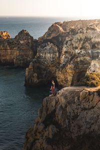 Man on rock by sea against sky