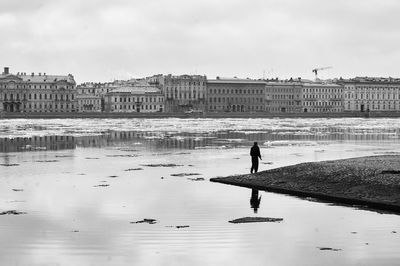 Man standing on frozen river by city against sky