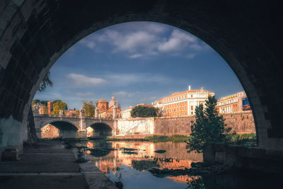 Bridge over river by buildings against sky