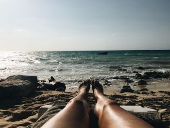 Low section of woman relaxing on beach against sky