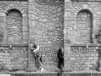 Side view of friends standing by stone wall