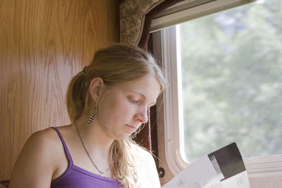 Young woman reading magazine while sitting by window in motor home