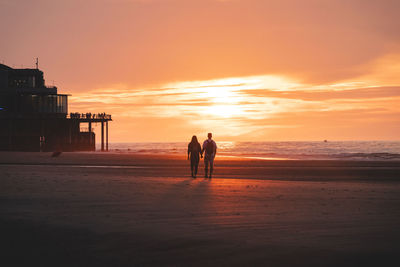 Silhouette woman walking at beach against sky during sunset