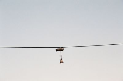 Low angle view of bird perching on cable against clear sky
