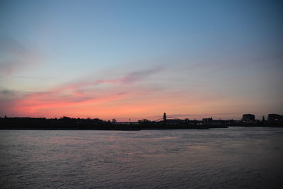 Silhouette buildings by sea against sky during sunset