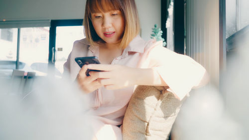 Woman using mobile phone while sitting on sofa at home