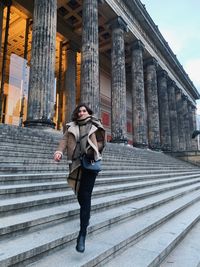 Full length portrait of woman moving down on steps against historic building