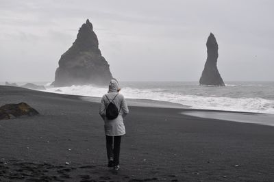 Rear view of man standing on beach against sky