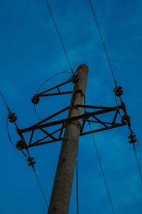 Low angle view of electricity pylon against blue sky