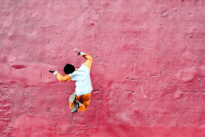 Rear view of playful boy jumping against old red wall