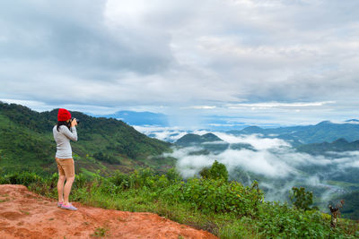 Woman photographing while standing on mountain against sky