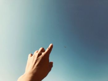 Cropped hand pointing at airplane flying against clear sky