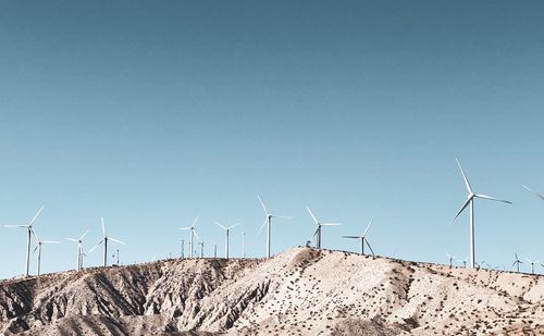 Wind turbines on land against clear sky