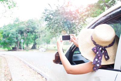 Woman photographing with mobile phone while traveling in car