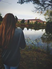 Rear view of woman standing by lake against sky